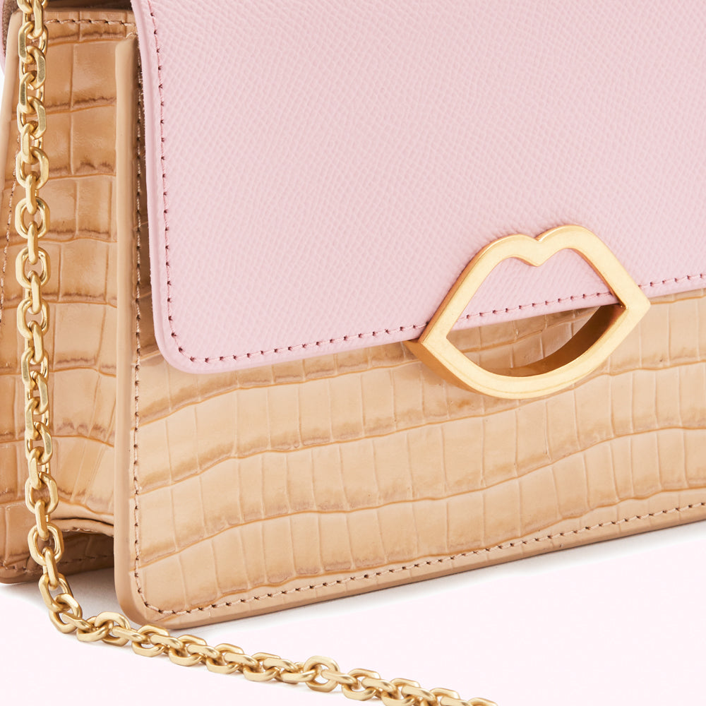 Close-up of a pink and beige crossbody bag with a gold lip-shaped detail.
