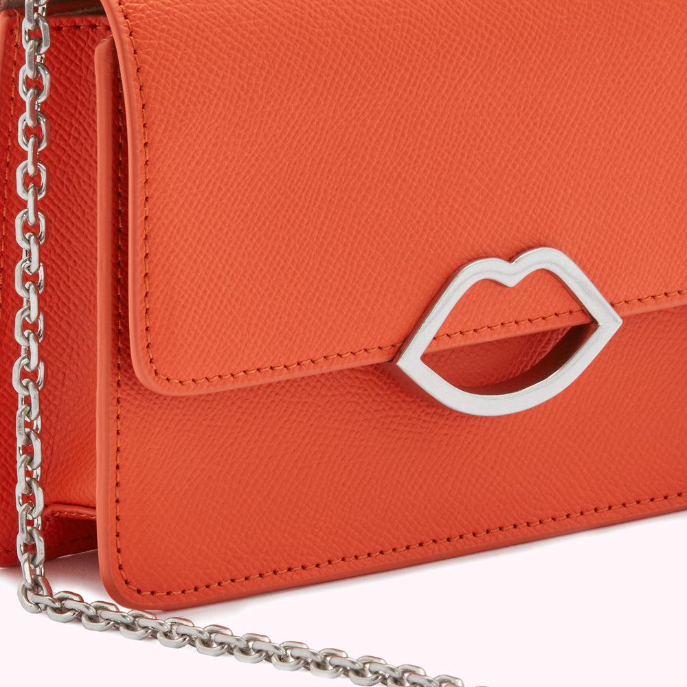 Close-up of a bright orange leather purse with a silver lip-shaped clasp and a silver chain strap.
