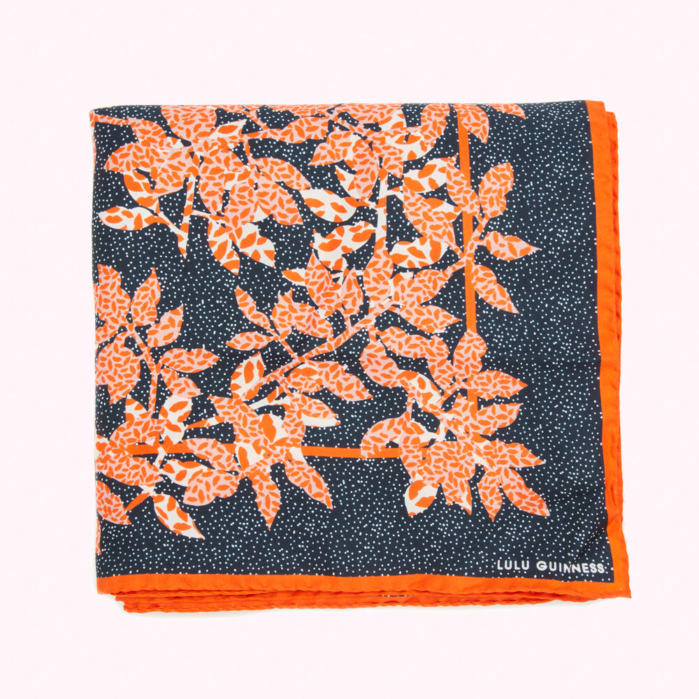 A folded Lulu Guinness silk scarf with an orange and navy leaf pattern on a white background.