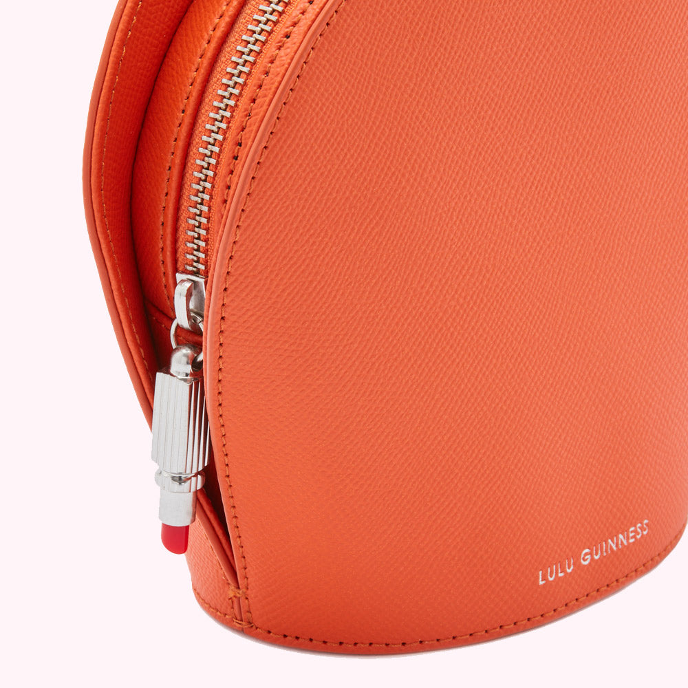 Close-up of an orange Lulu Guinness bag with a silver zipper and a red and silver zipper pull.

