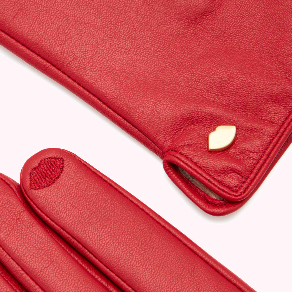 Close-up of a pair of red leather gloves with a small gold lip-shaped detail.
