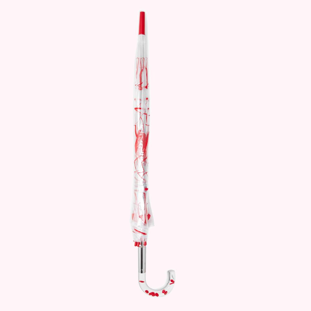 A closed clear umbrella with a red handle and red design.