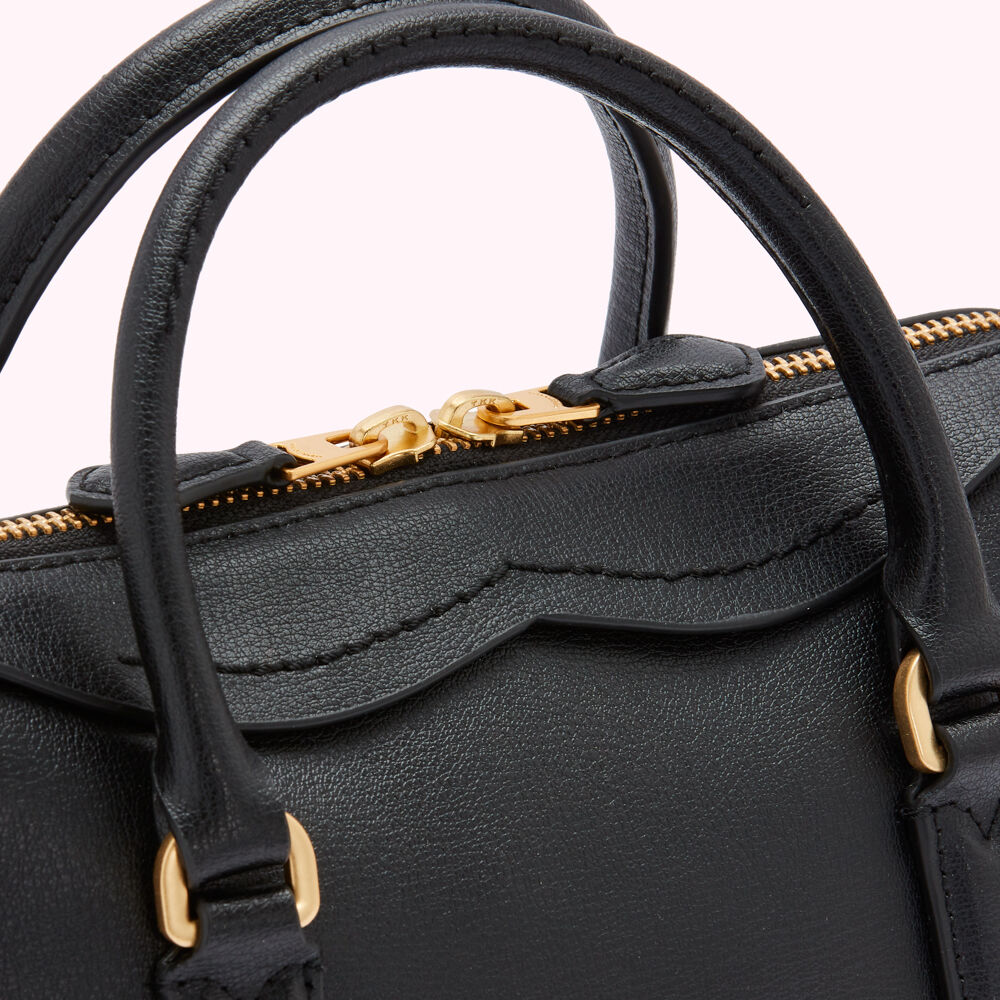Close-up of a black leather handbag with gold zipper and handles.
