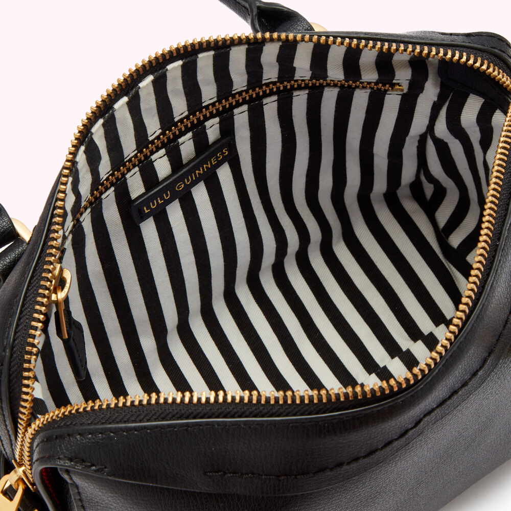 Interior of a black Lulu Guinness handbag with a black and white striped lining and gold zipper.
