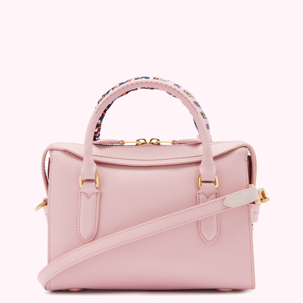Pink leather handbag with a patterned fabric handle and a long shoulder strap.

