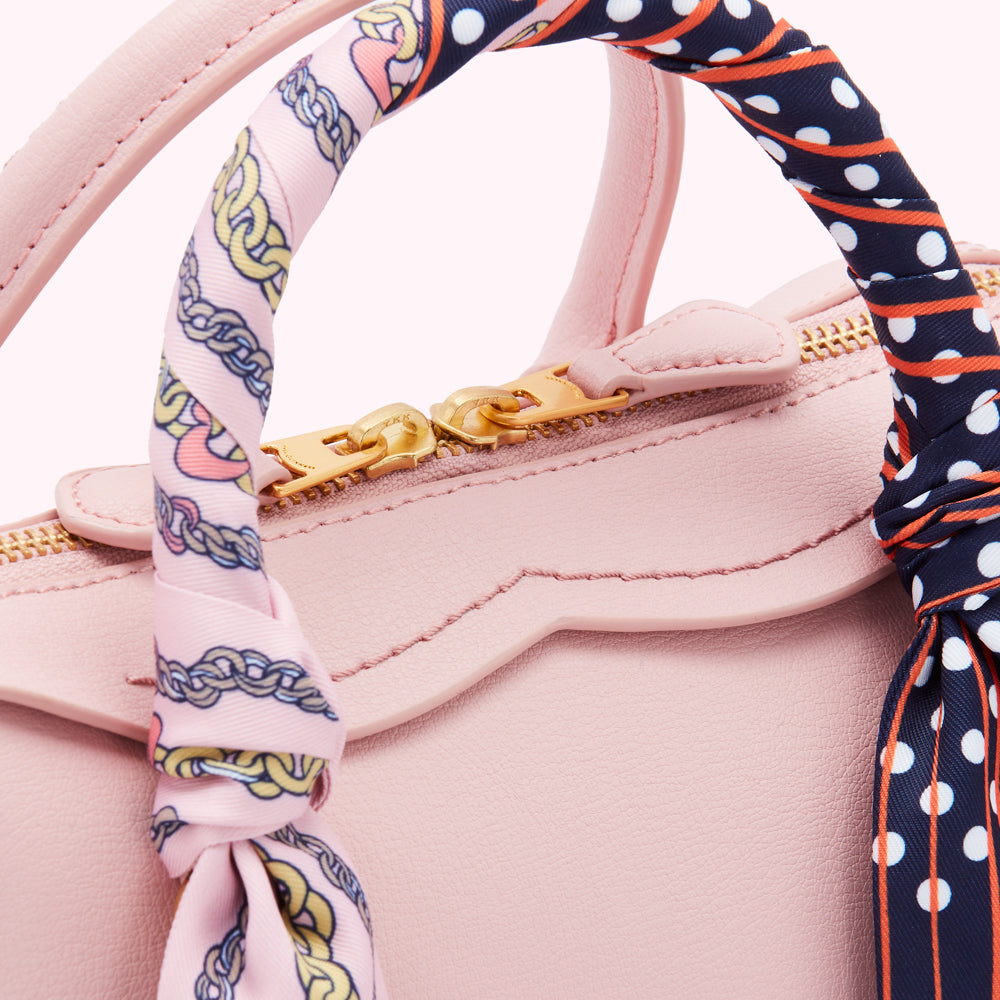 Close-up of a pink handbag's top handle and zipper, adorned with a patterned scarf.
