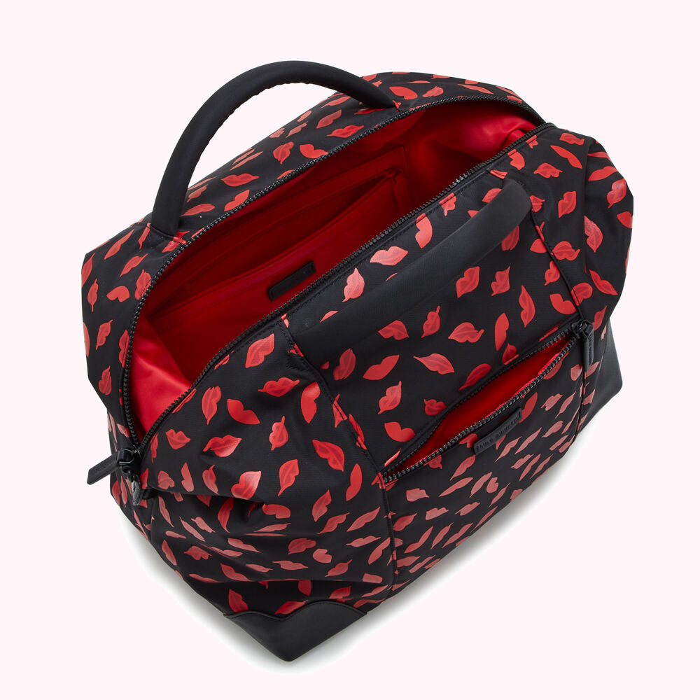 Black duffel bag with a red lipstick print, shown open to reveal a red interior with multiple compartments.
