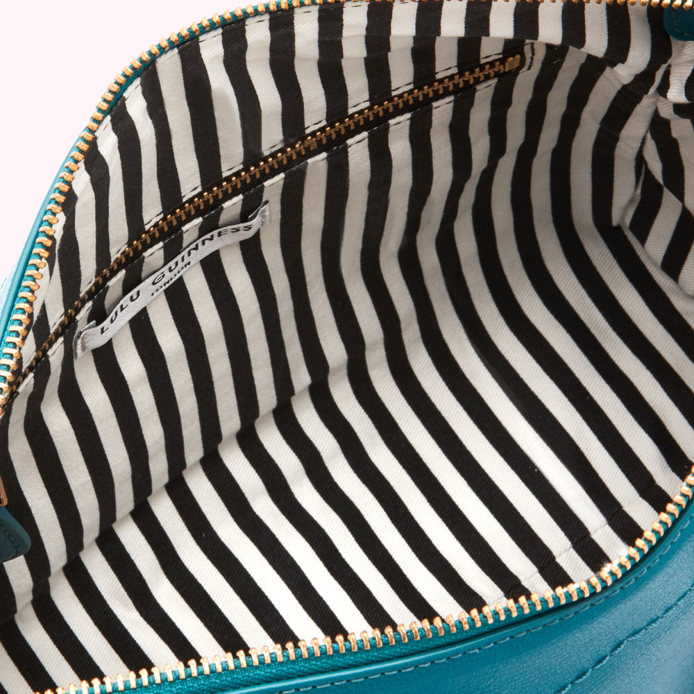 Interior of teal Lulu Guinness bag with black and white striped lining and gold zipper.
