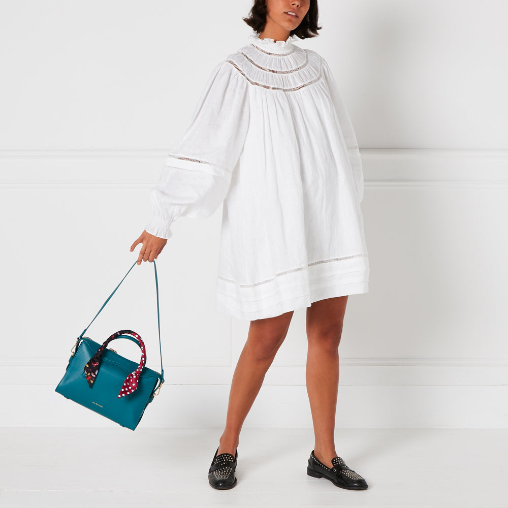 Woman in white dress holding teal handbag against white background.