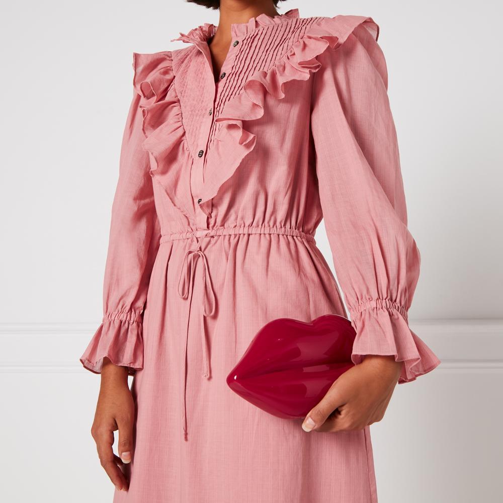Woman in a pink dress holding a red lip-shaped clutch.
