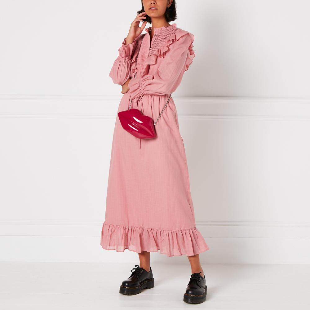A woman in a pink dress and black shoes carries a red lip-shaped purse against a white background.