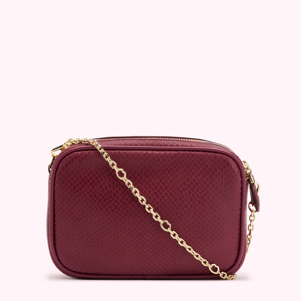 A burgundy rectangular crossbody bag with a gold chain strap and snakeskin embossed texture.
