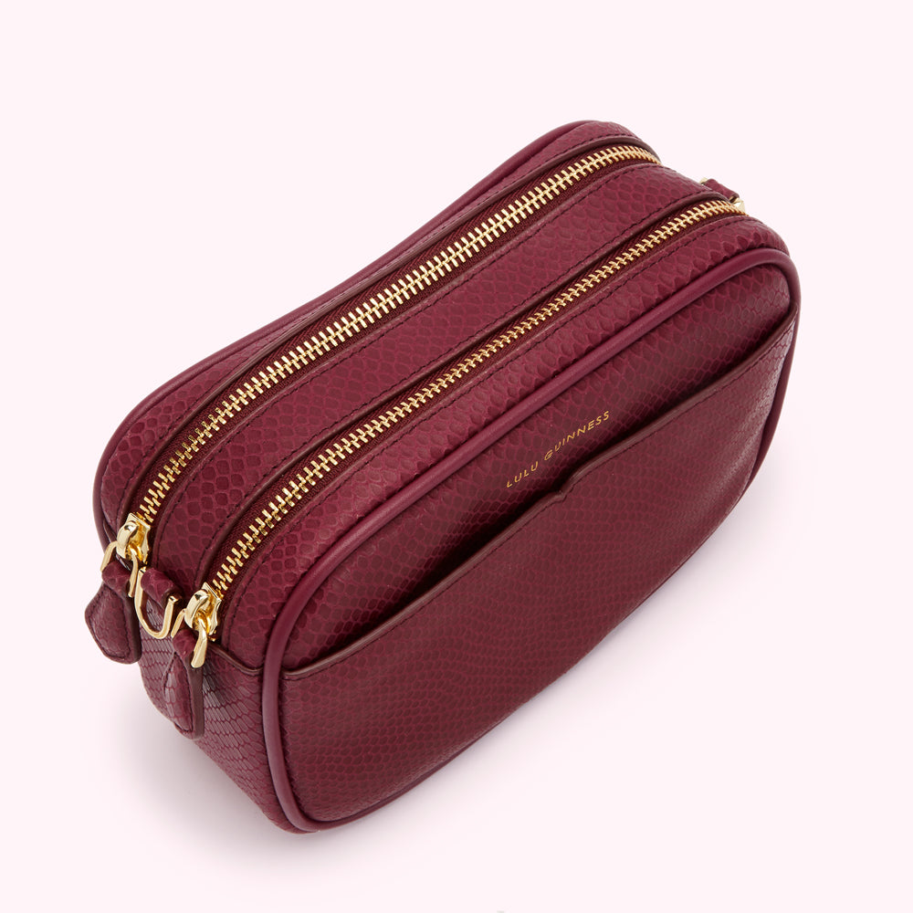 A burgundy Lulu Guinness crossbody bag with two gold zippers.