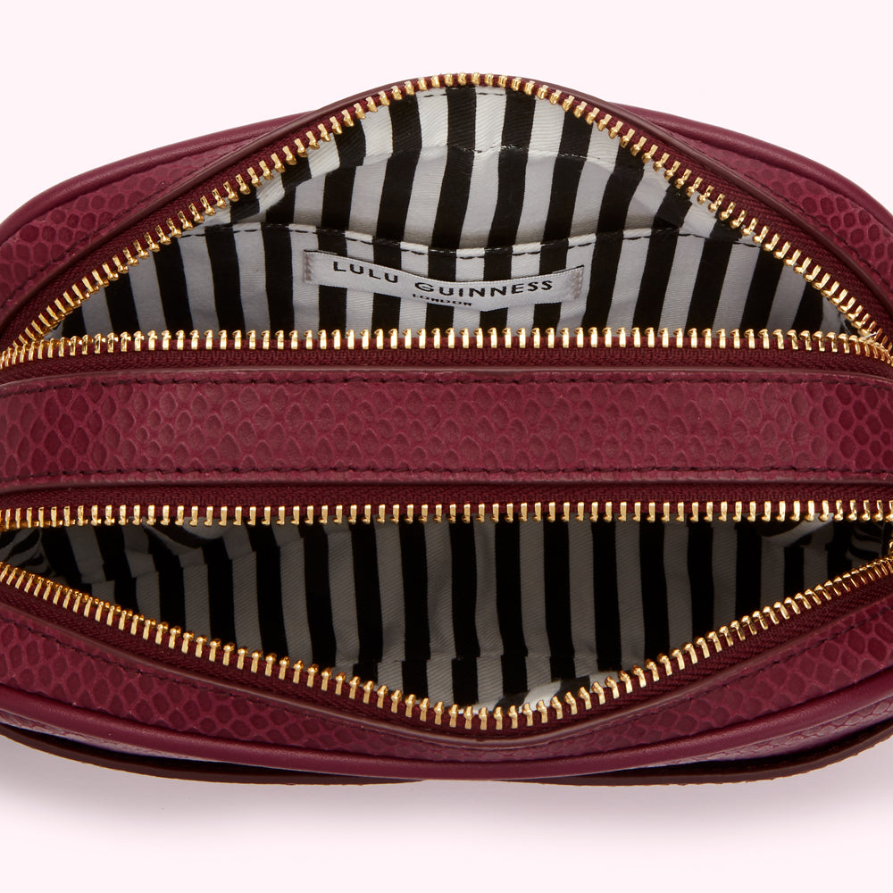 Interior of a burgundy Lulu Guinness purse with gold zippers and a black and white striped lining.