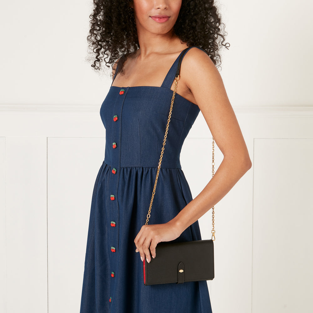 Woman in a denim dress holding a black chain wallet.
