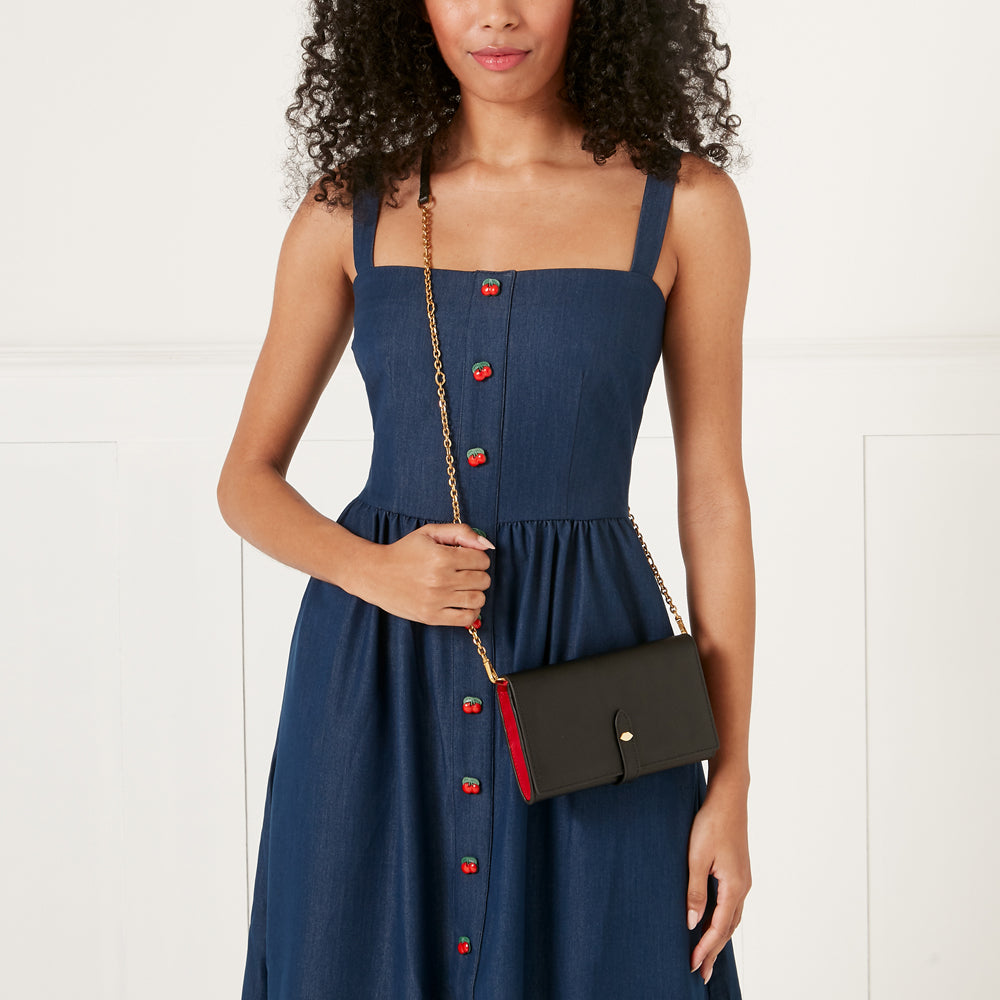 A woman in a dark blue cherry-button dress holds a black and red wallet-on-a-chain.