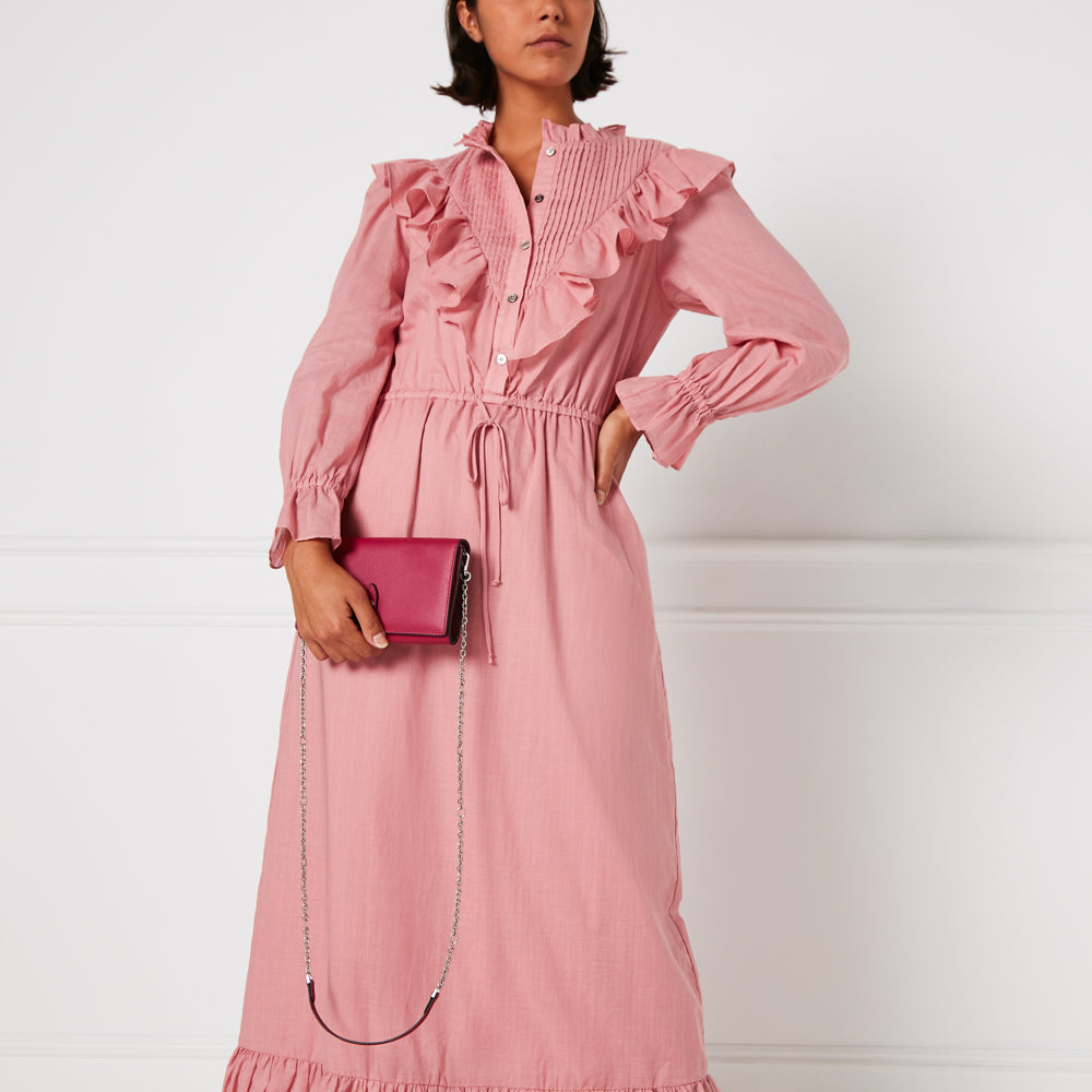 A woman in a pink dress holds a burgundy crossbody purse with a silver chain strap against a white background.