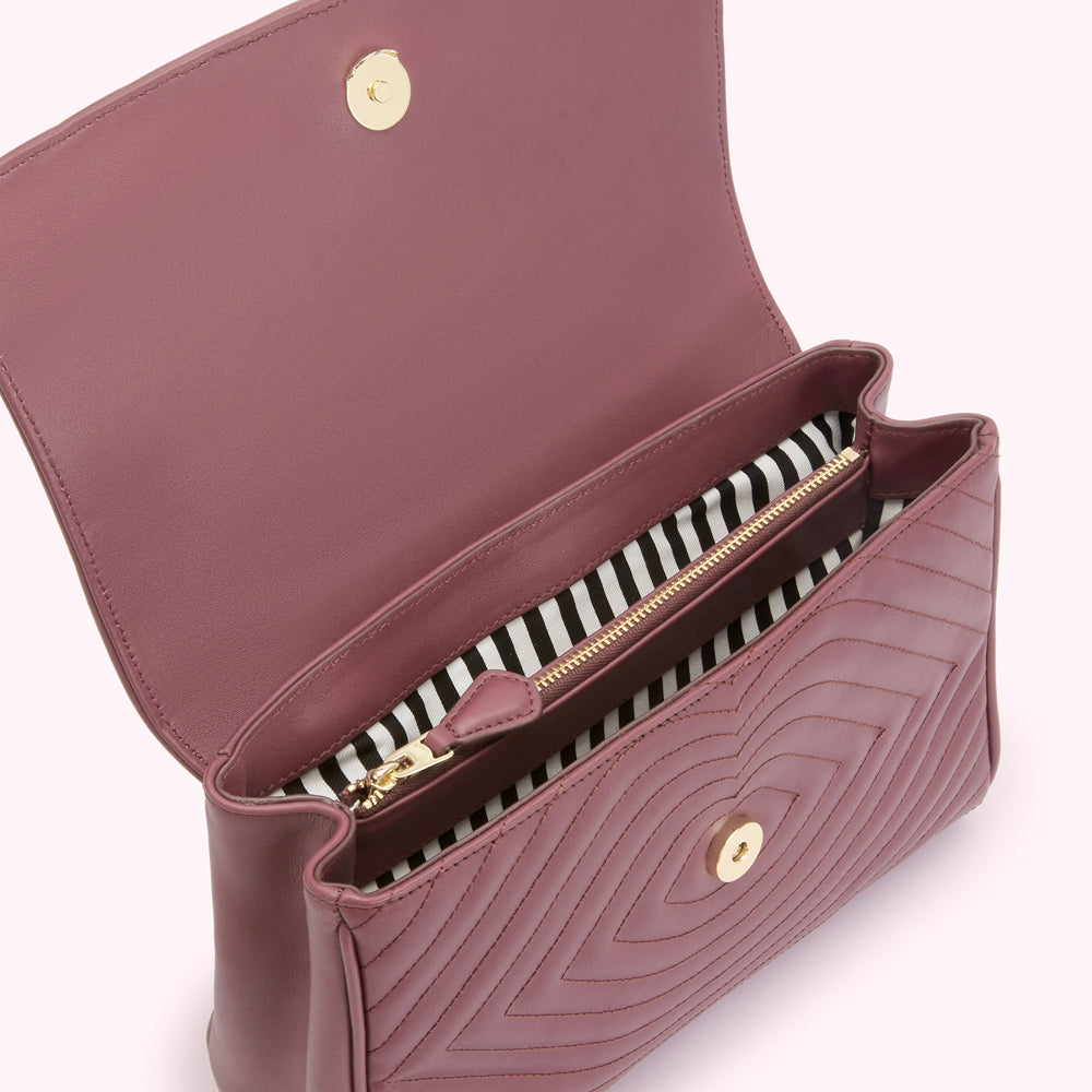 A dusty rose quilted handbag is open to reveal its black and white striped interior.
