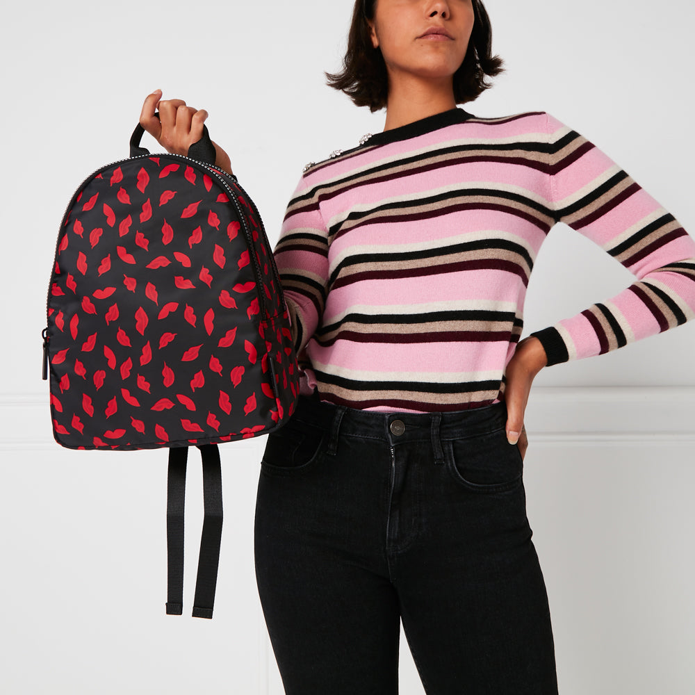 Woman holding a black backpack with red lips print against a white background.