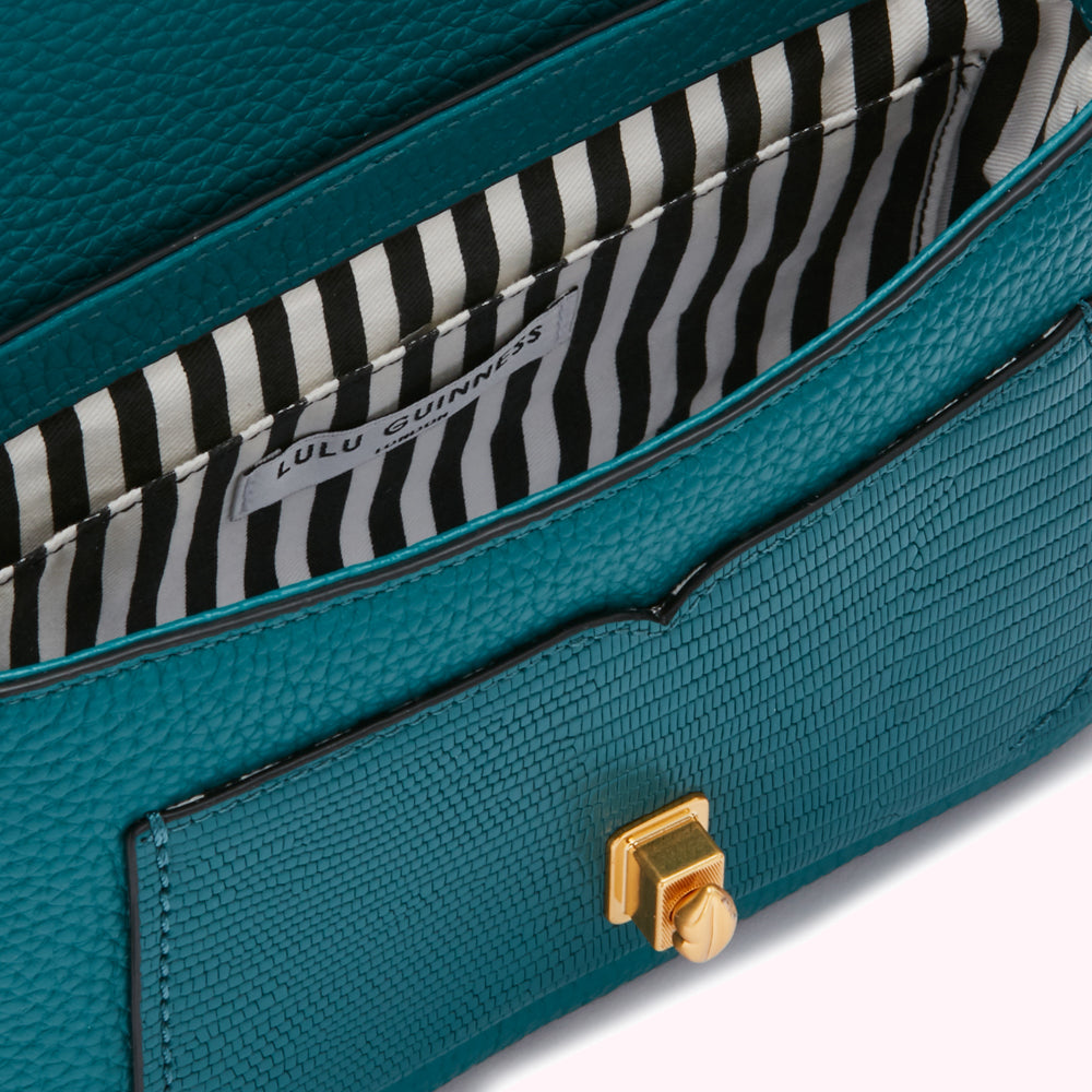 Close-up of the teal interior of a Lulu Guinness handbag, showing the black and white striped lining and gold clasp.
