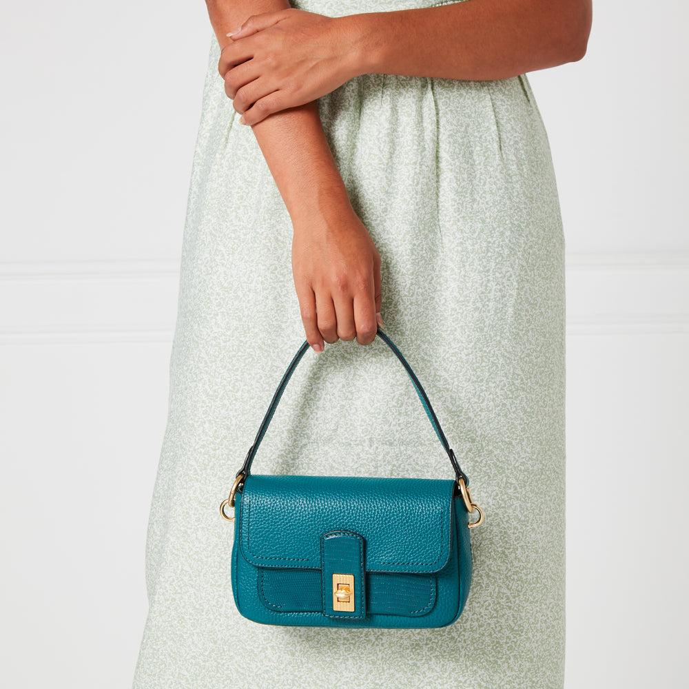 Woman holding teal baguette bag against a white background.
