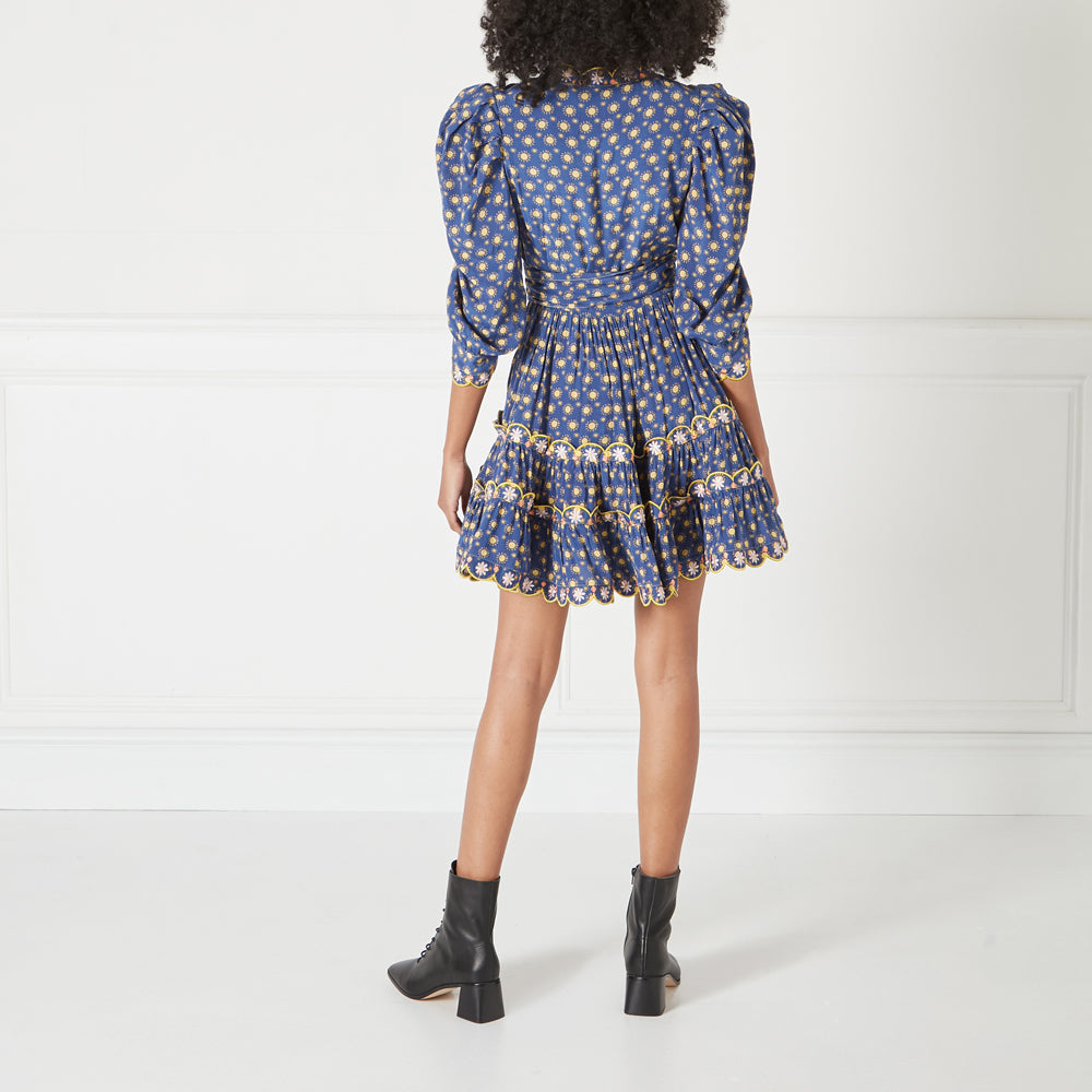 Rear view of a woman wearing a blue floral mini dress with puff sleeves and black ankle boots.
