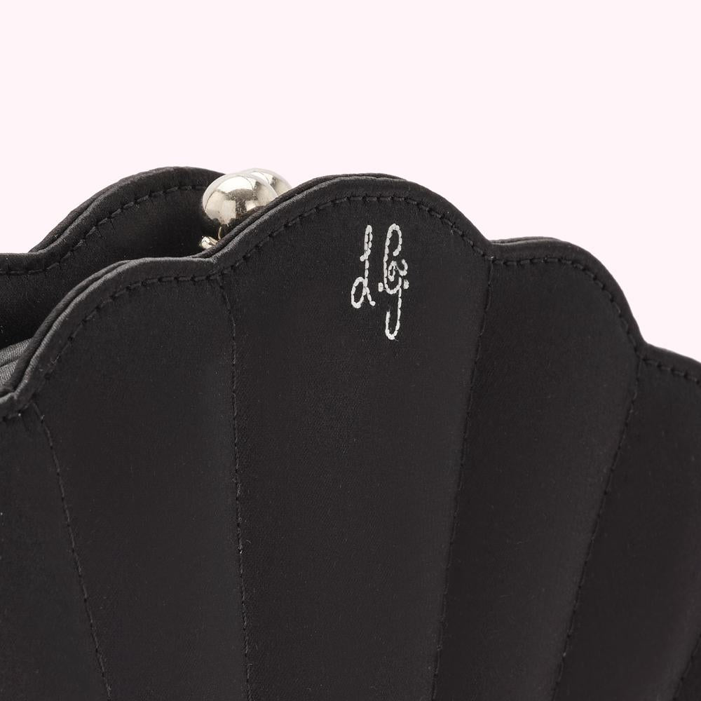 Close-up of a black, seashell-shaped clutch with the designer's logo embroidered in white.
