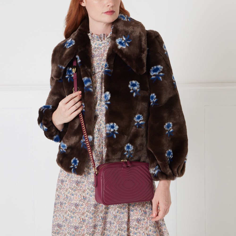 Woman wearing a brown floral faux fur jacket and a patterned dress, holding a burgundy quilted crossbody bag.