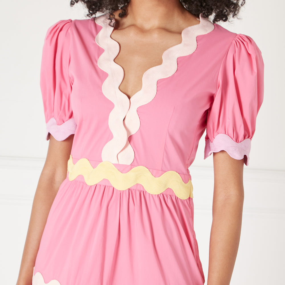 Close-up of a pink dress with pastel yellow and lavender scalloped trim.
