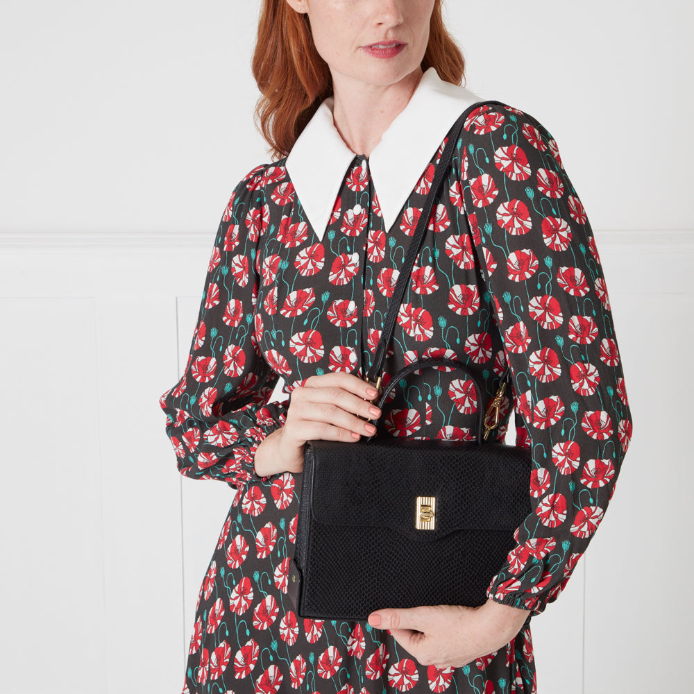 Woman in poppy print dress holding a black handbag.
