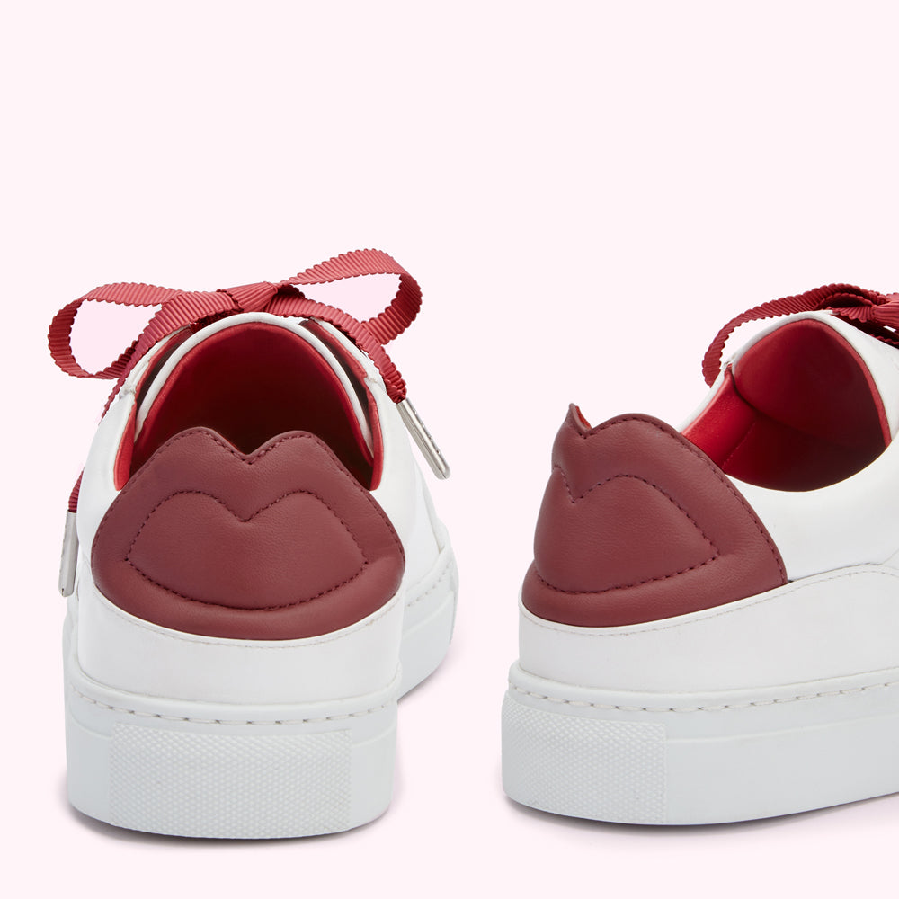 Pair of white leather sneakers with burgundy lip-shaped heel detail and burgundy ribbon laces, on a white background.
