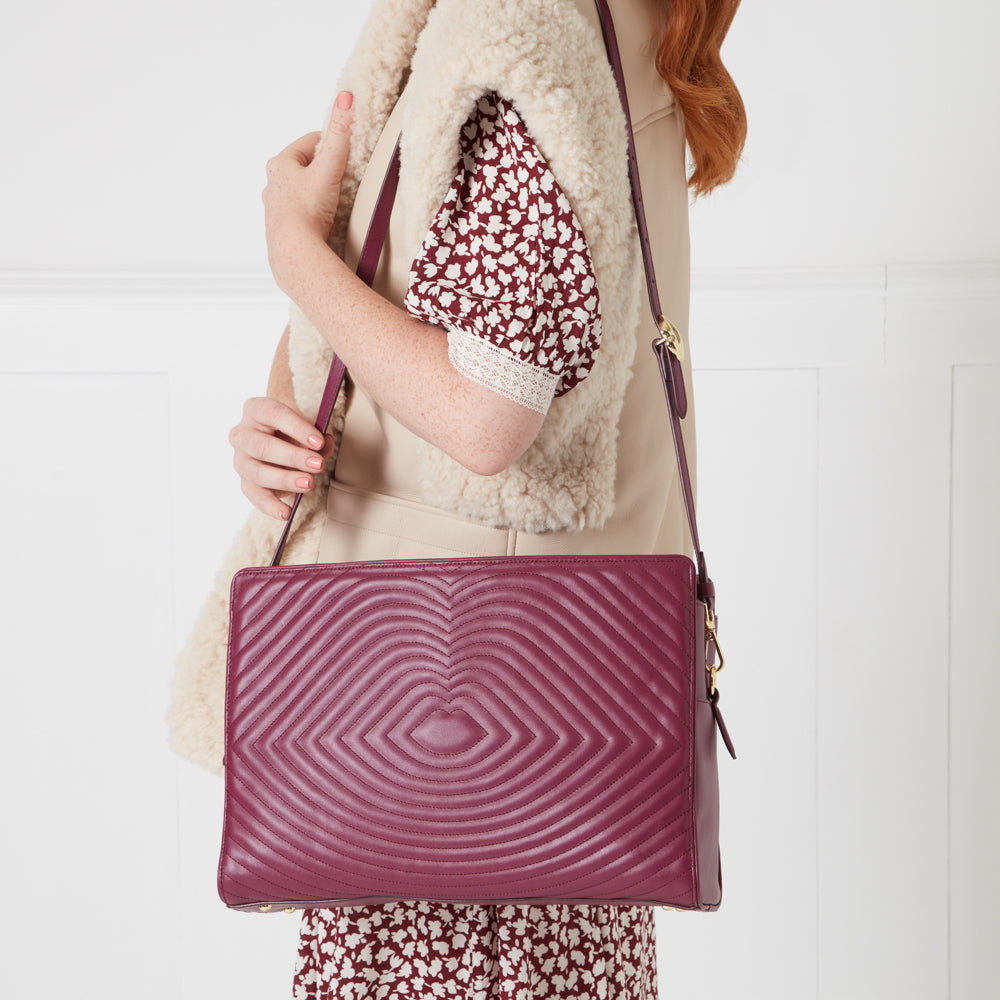 Woman's maroon quilted leather crossbody bag with a beige sherpa vest and floral dress.
