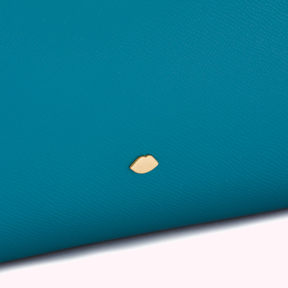Close-up of teal leather with a gold lip emblem.
