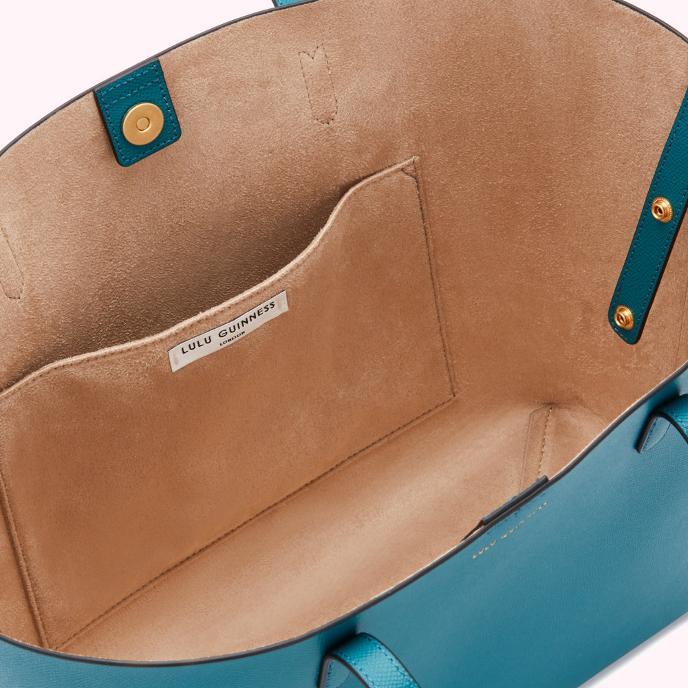 Inside of teal Lulu Guinness tote bag with beige lining and small interior pocket.