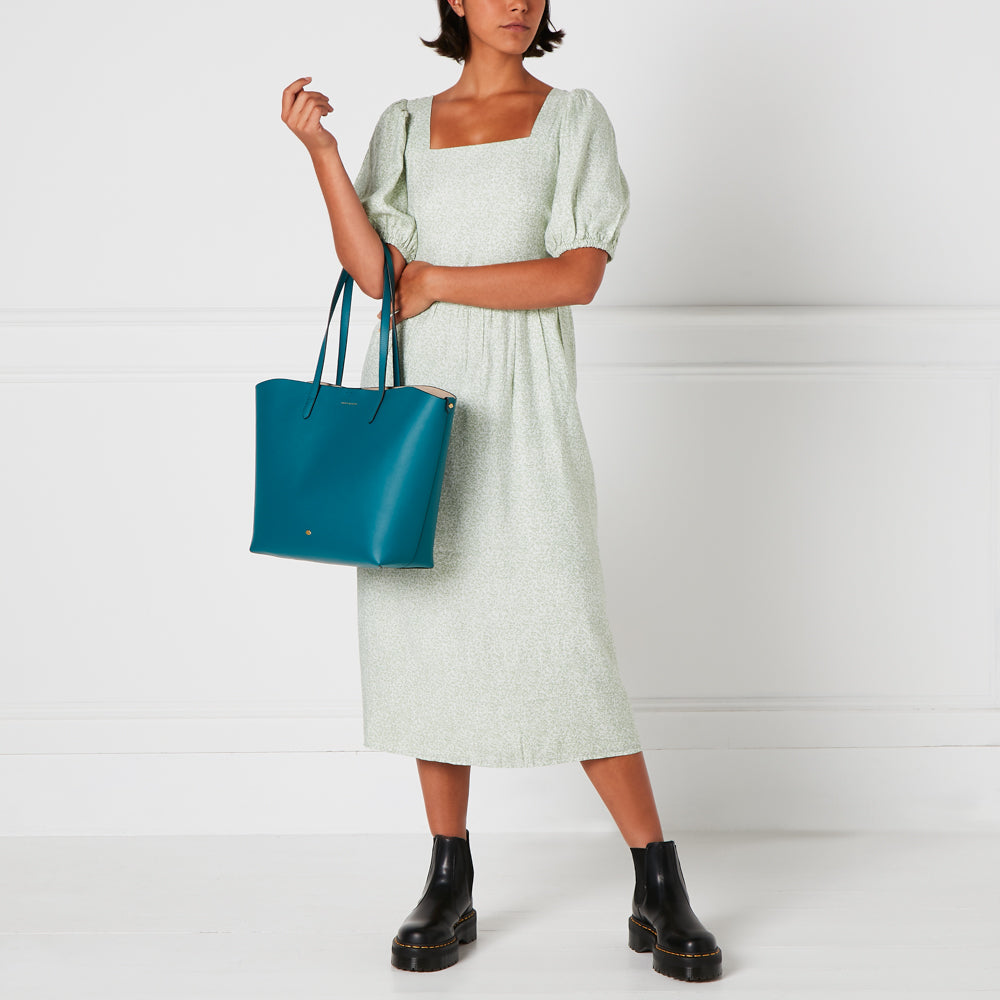 Woman in a light green dress holding a teal tote bag.
