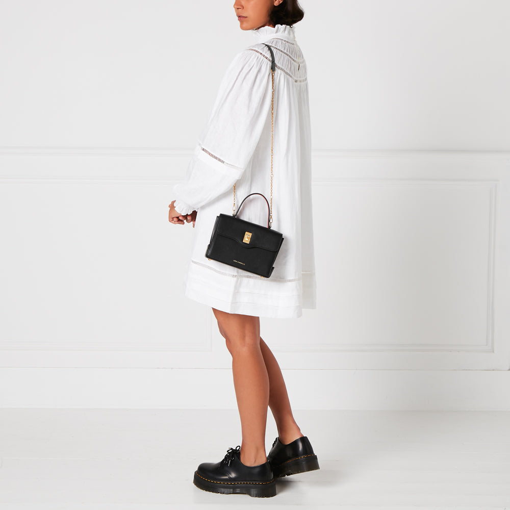 A woman in a white dress carries a black crossbody bag with gold hardware.