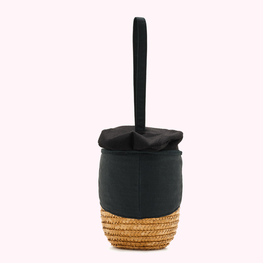 Black fabric handbag with a straw bottom and a single top handle, shown from the back.
