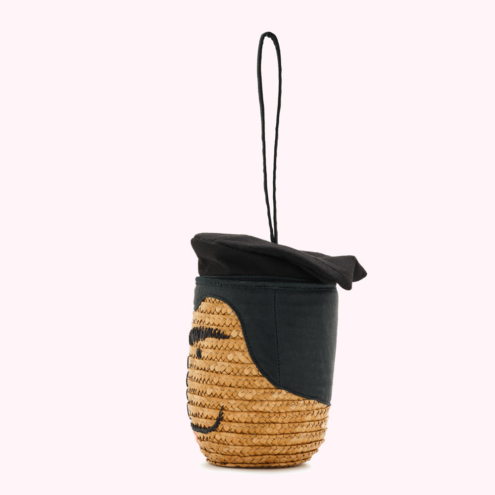 A tan woven straw bag shaped like a face wearing a black beret. The bag has a black fabric strap.