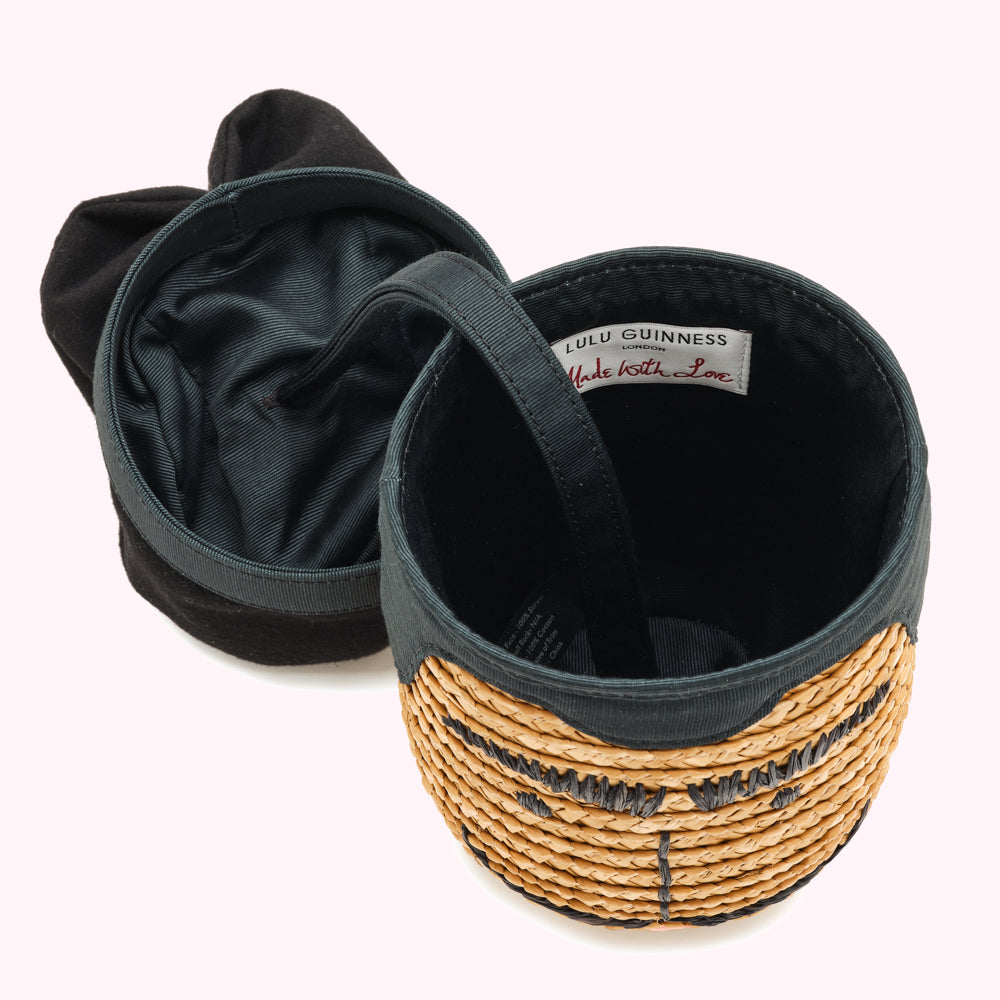 A dark green Lulu Guinness hat with a straw face and black ears, turned inside out to show the interior lining and label that reads "Made with Love".
