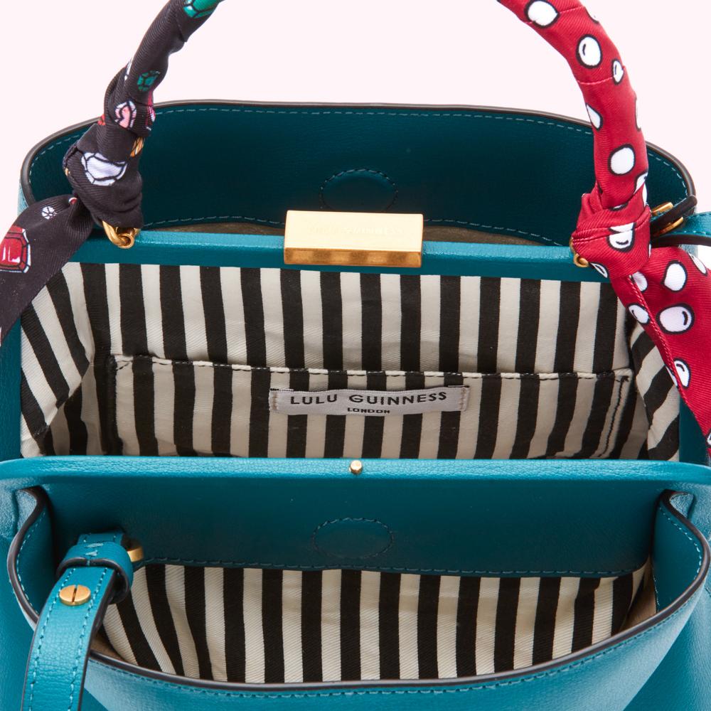 Teal Lulu Guinness handbag open to reveal black and white striped lining and a label reading "Lulu Guinness London". The handbag has a red and white polka dot and jewel-toned patterned scarf handle.
