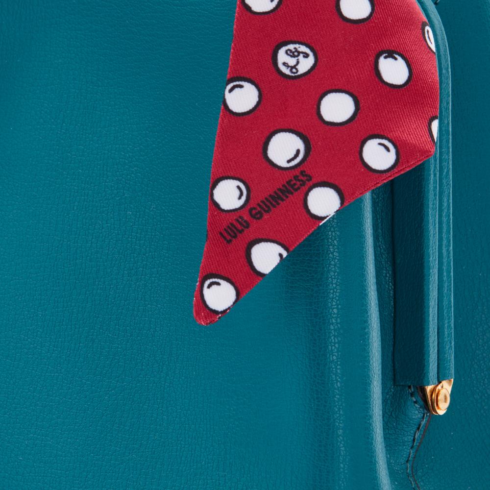 Close-up of a teal Lulu Guinness bag with a red and white polka dot scarf detail.
