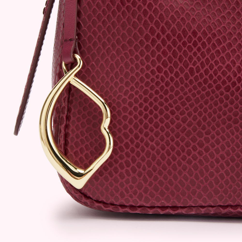 Closeup of a burgundy purse with a gold heart-shaped clasp. The purse is made of textured leather.