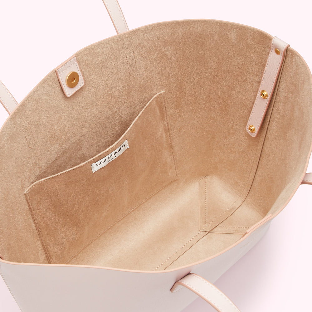 Inside of a pale pink Lulu Guinness tote bag, showing the beige lining and interior pocket.
