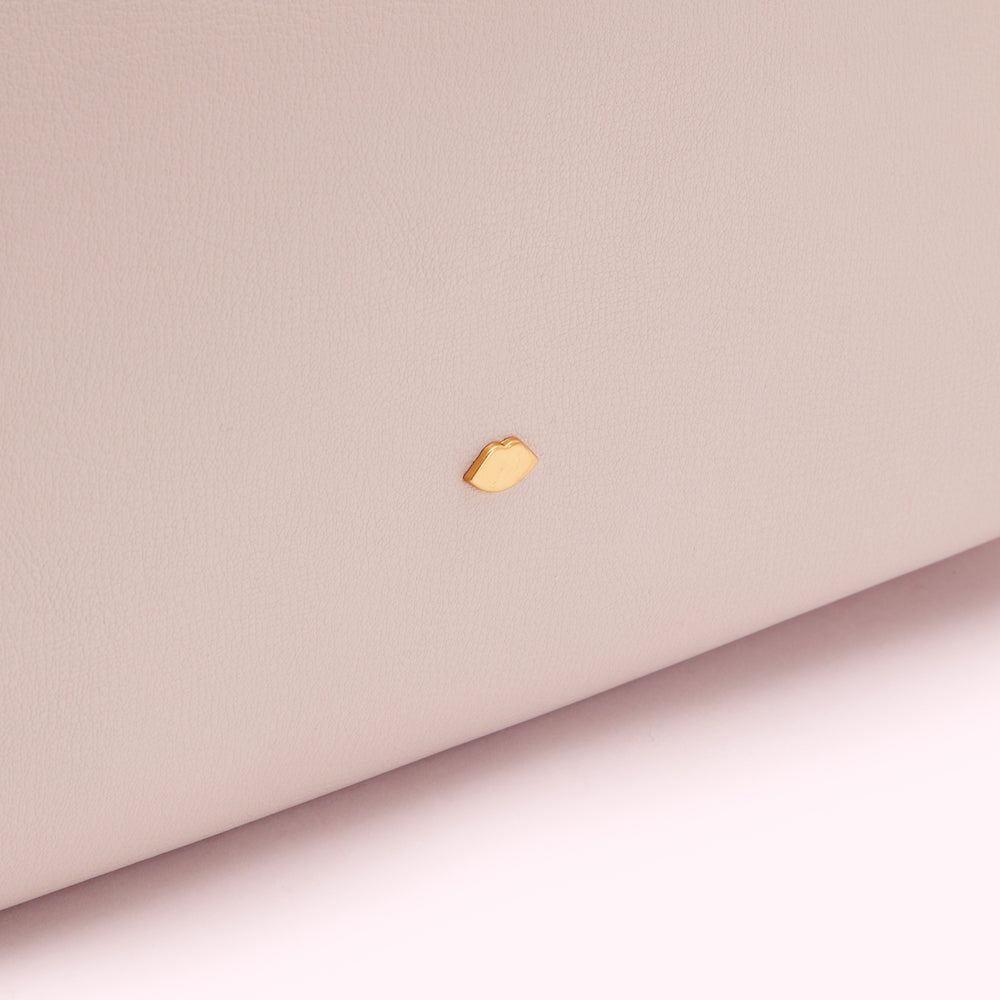 Close-up of a pale pink leather surface with a small gold lip-shaped emblem.
