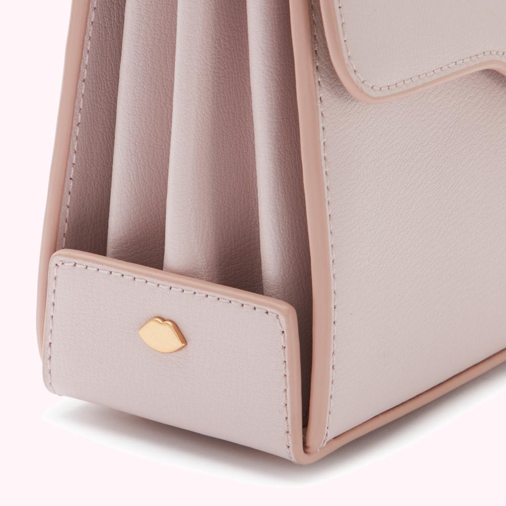 Close-up of a pale pink leather handbag with a gold lip-shaped detail.
