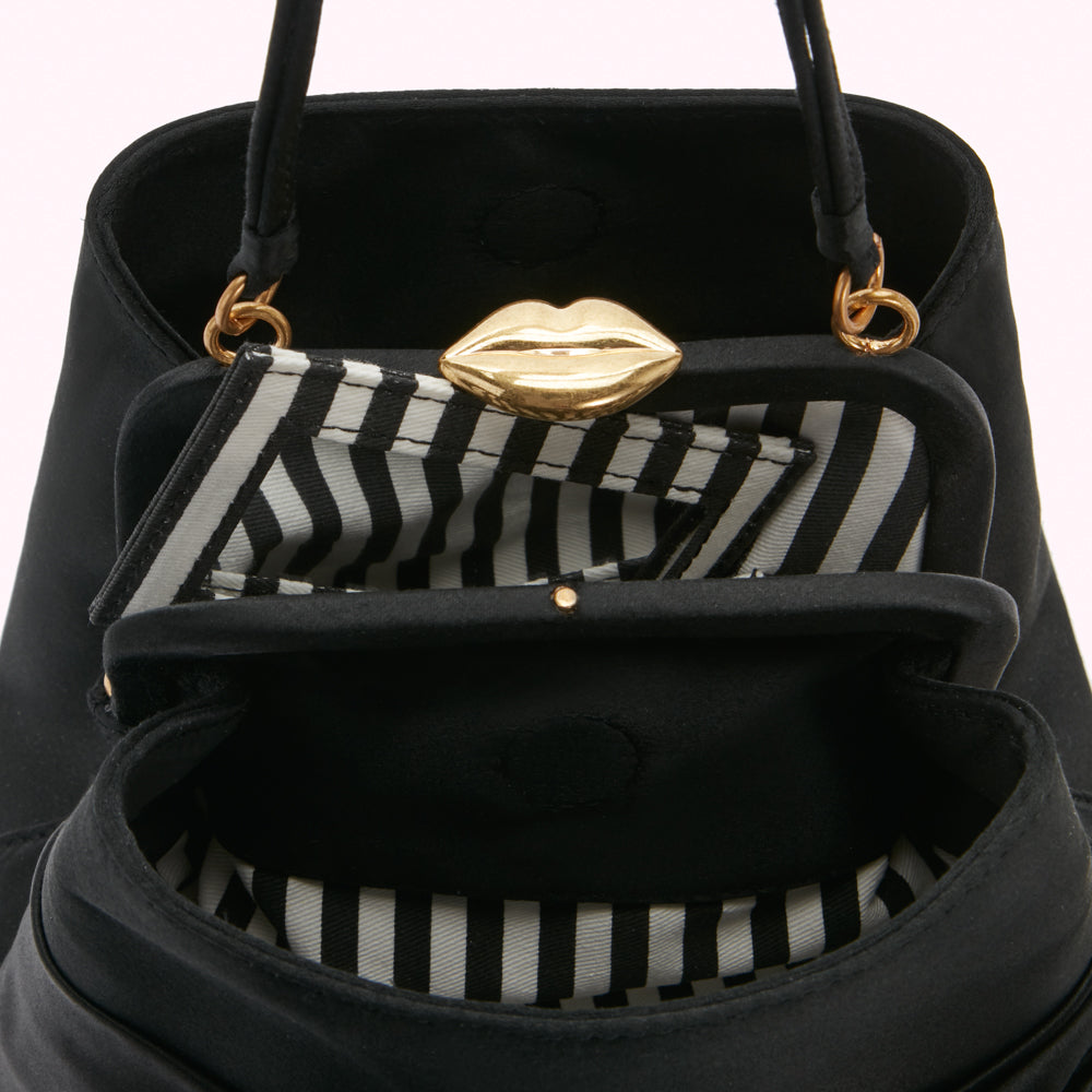 Close-up view of the inside of a black satin handbag with a gold lip-shaped clasp and black-and-white striped lining.
