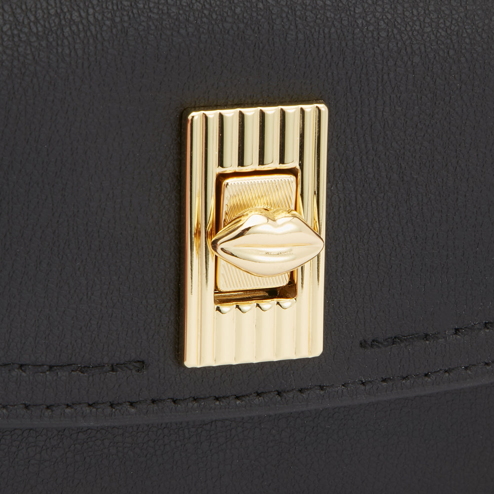 Close-up of a black purse's gold clasp featuring a lip-shaped detail.
