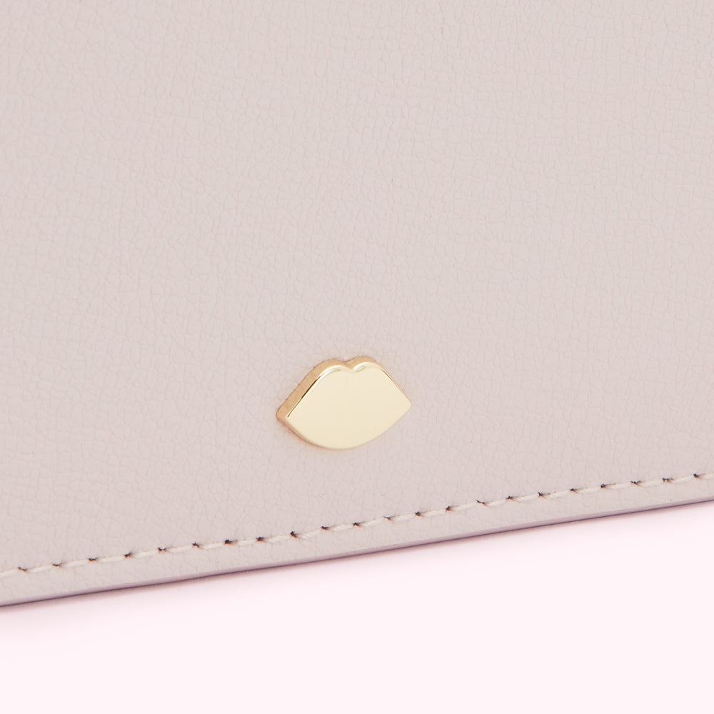 Close-up of a pale pink leather purse with a gold lip-shaped emblem.