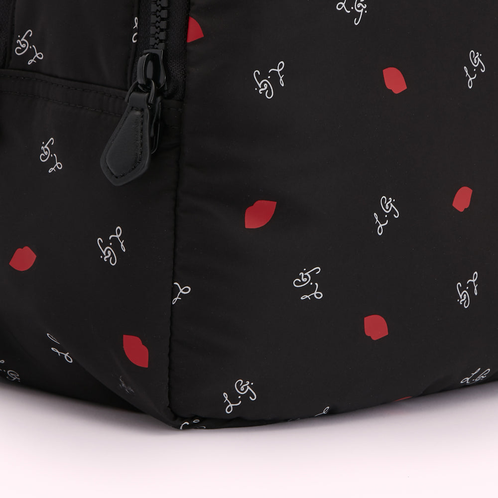 Close-up of a black backpack with a red lips and cursive writing pattern.
