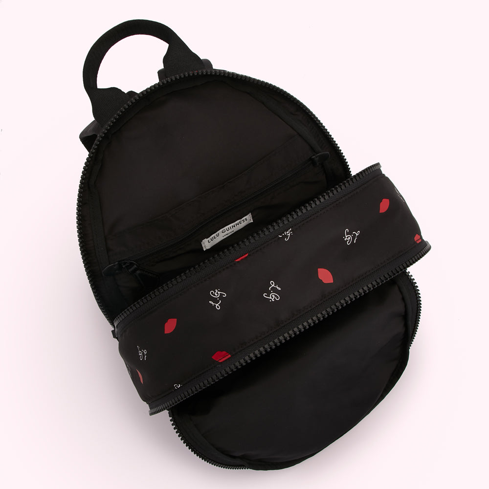 Black Lulu Guinness backpack open to reveal a red lips and logo print lining.